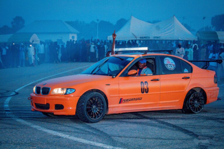 Bright orange car drifting during nighttime racing event with enthusiastic crowd.